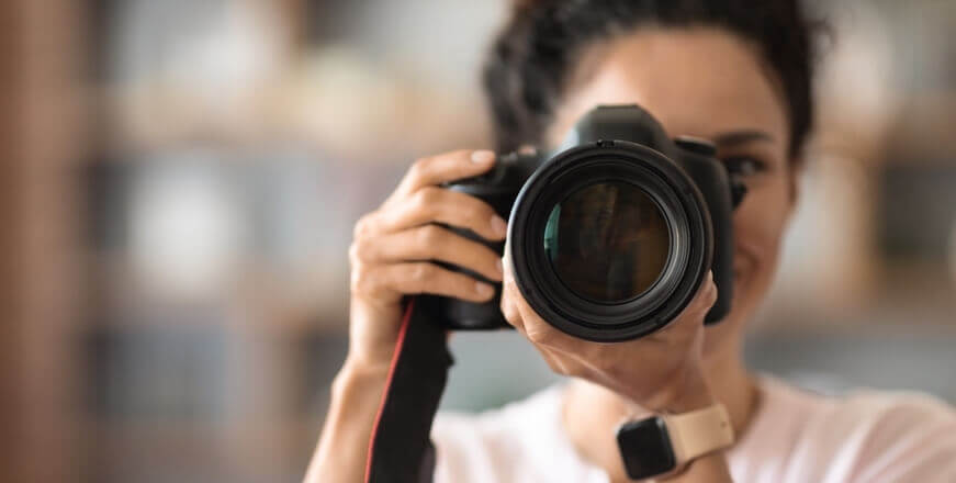 Image of a female holding a large black camera taking a photograph.