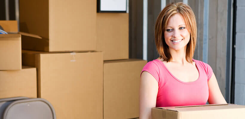 Woman in pink shirt looking happy holding boxes moving house