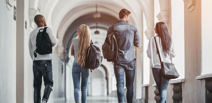 Image of students with rucksacks walking down a long corridor. 