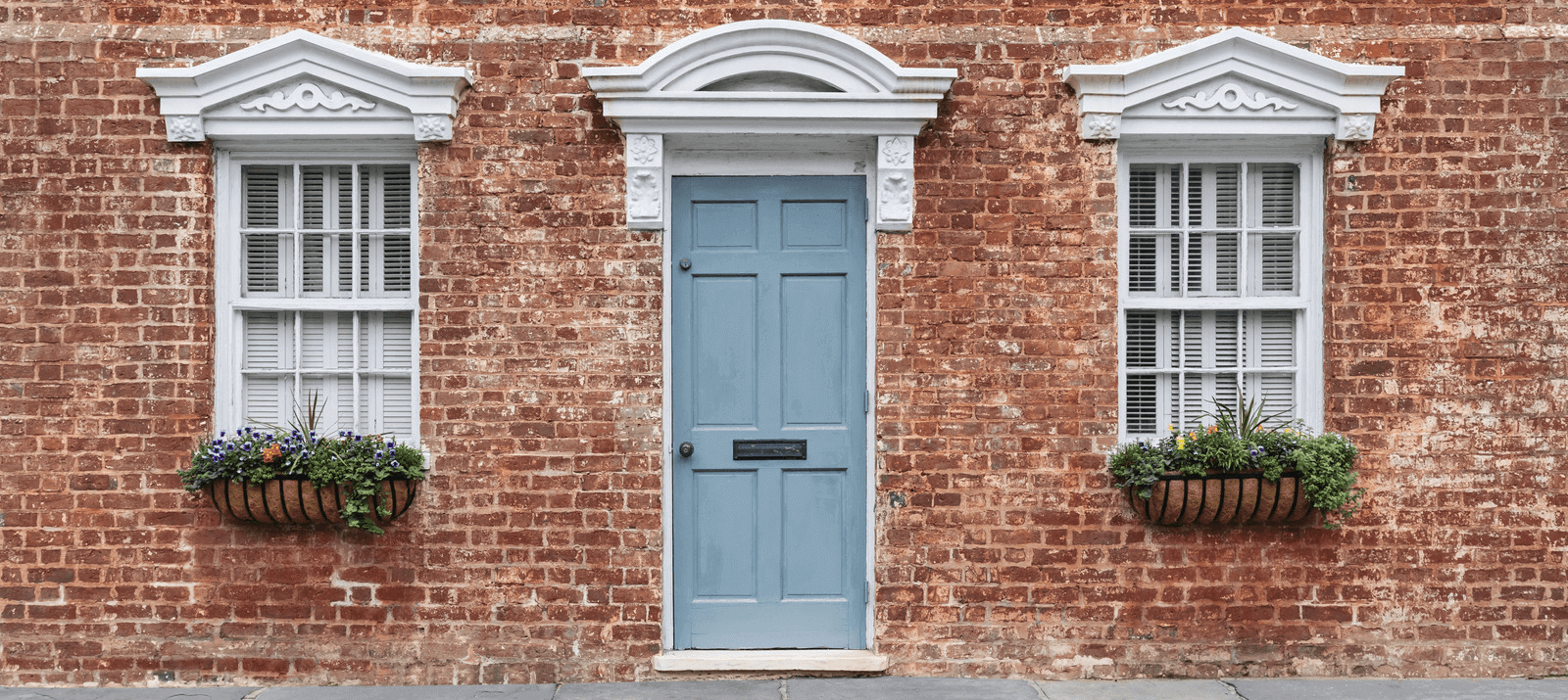 A blue front door on a red brick house, flanked by traditional windows with window boxes.