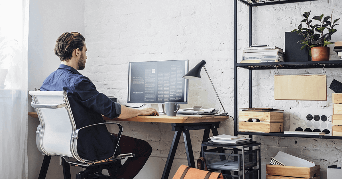 man sitting at wooden desk in a home office environment. shelving next to the desk stacked with organised paperwork and documents