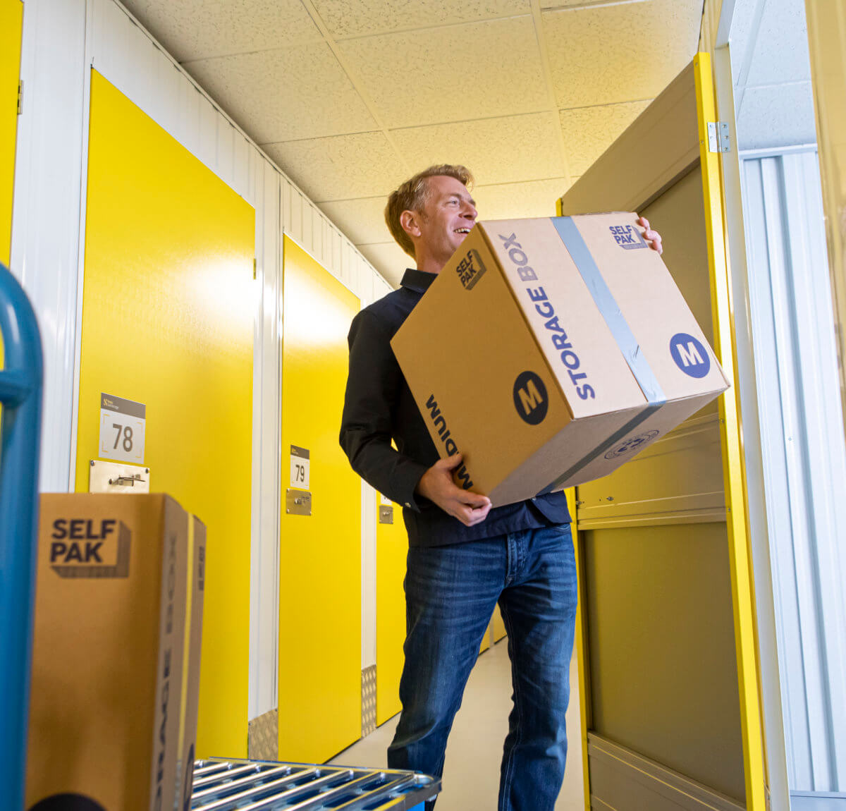 man moving boxes from blue trolley into yellow storage unit