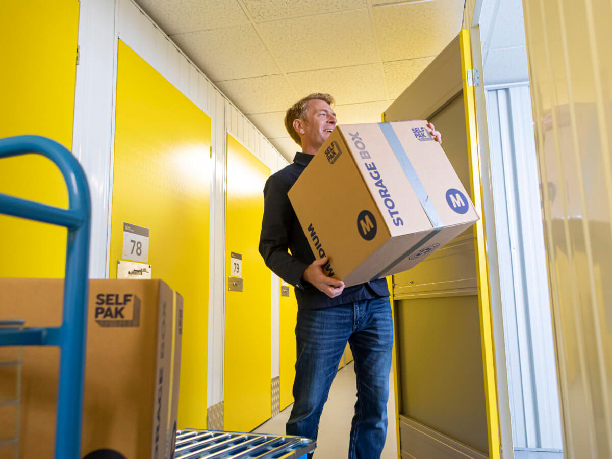 man moving boxes from blue trolley into yellow storage unit