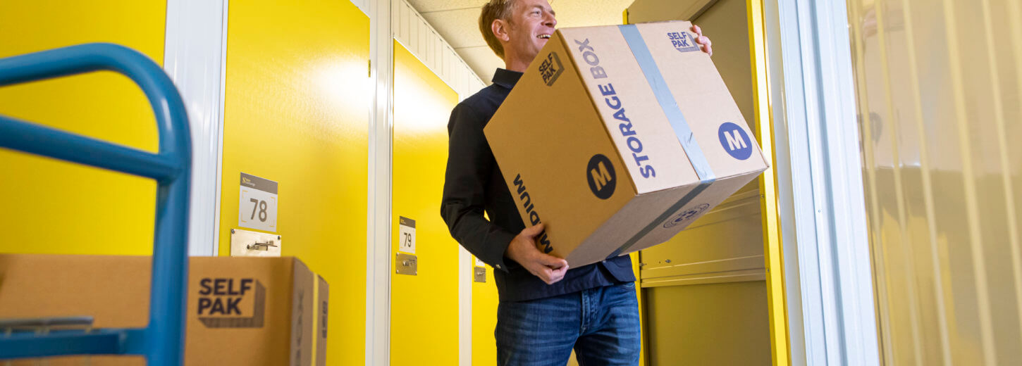 man moving boxes from blue trolley into yellow storage unit