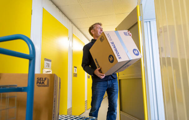 man moving boxes from blue trolley into yellow storage unit