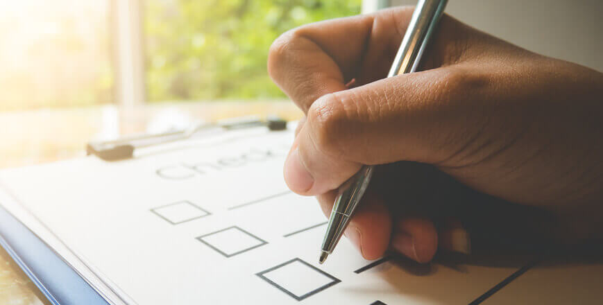 Image of a biro pen with a hand holding it filling out square boxes on a checklist.