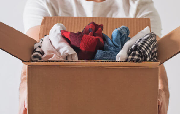 Image of man holding cardboard box full of folded clothes.