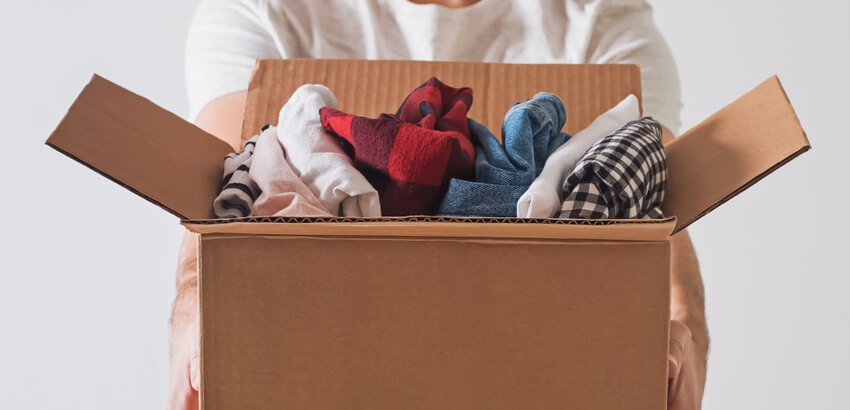 Image of man holding cardboard box full of folded clothes.