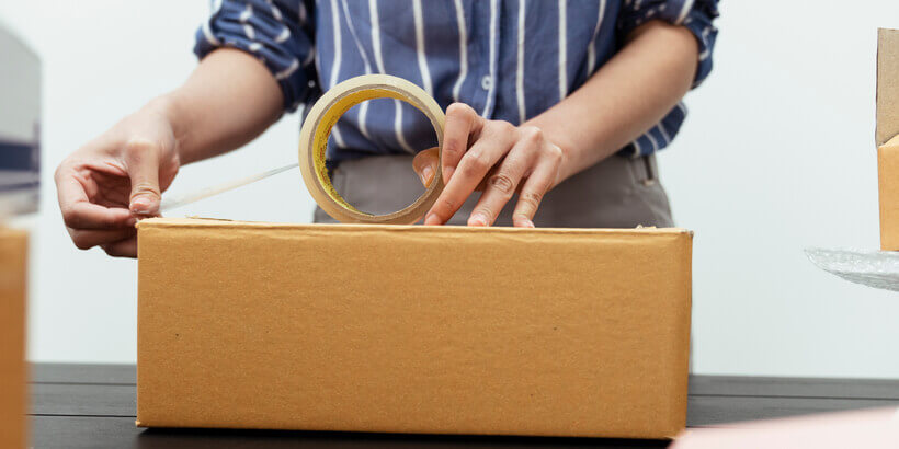 Image of man sellotaping cardboard box so it's sealed. 