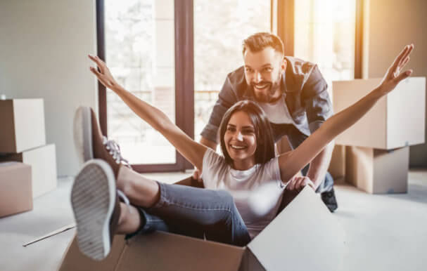 Image of a man and a woman happy while the woman sits laughing in empty cardboard storage box in new home.