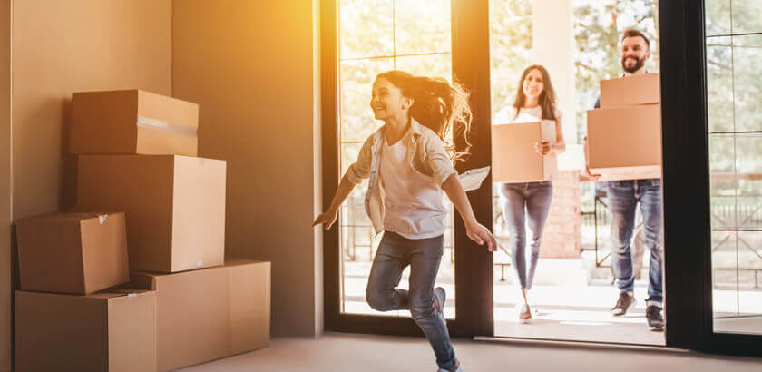 Image of child running into new home with parents behind holding cardboard boxes containing possessions.