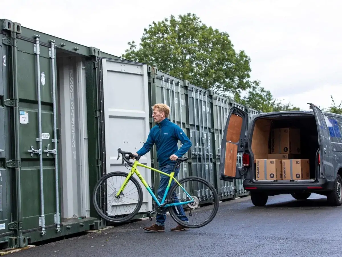 A man carrying a bicycle into a green storage container