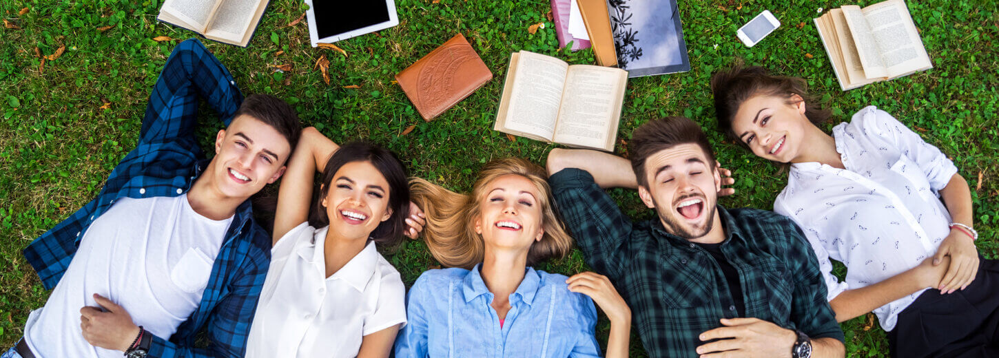 Students lying on their backs on the grass with books lying around.