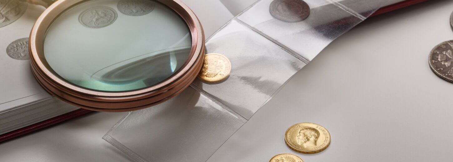 Antique collectable coins on a table with a book and a magnifying glass.
