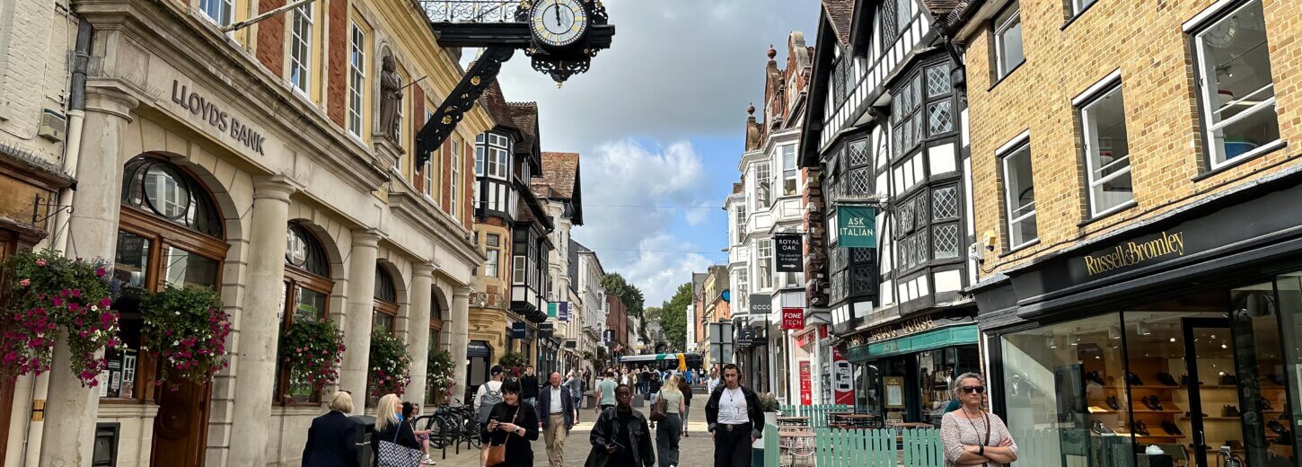 An image of winchester town centre with people walking through the centre and shops surrounding them.