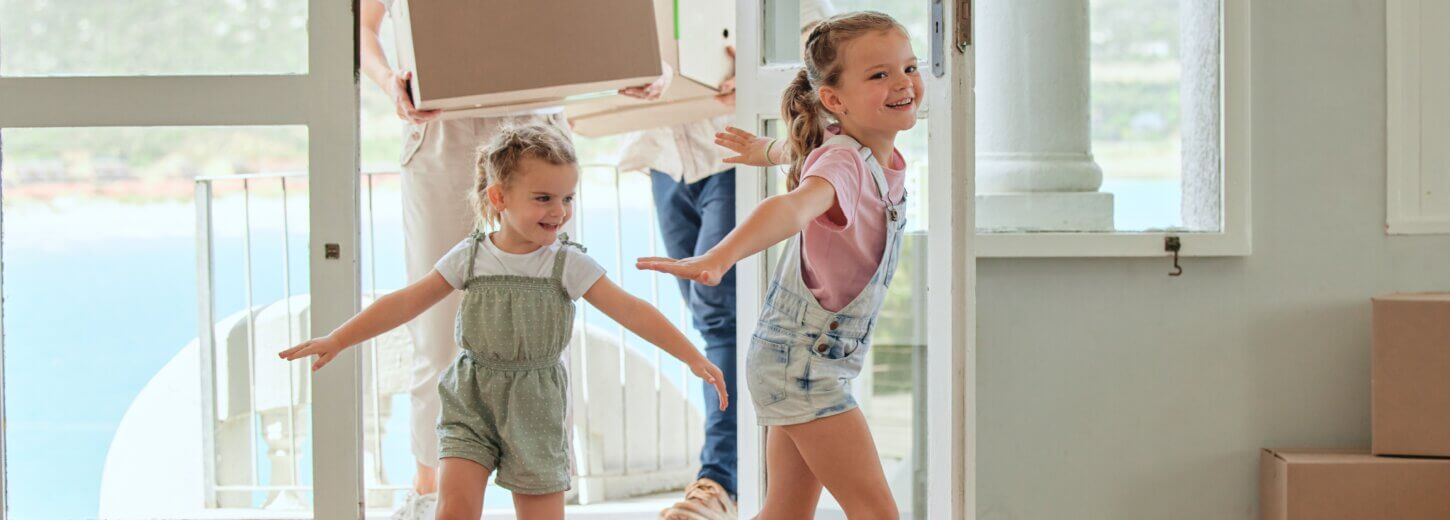 An image of a family moving into their new home in Newbury with two parents holding boxes and two children running through the door.
